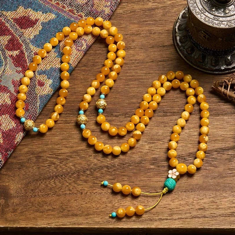 Coiled amber prayer beads necklace flat lay showing turquoise and gold accent beads against wooden surface with vintage decor