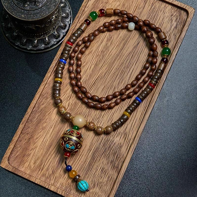 Tibetan handmade mala necklace with copper beads and schima wood, flat lay on wooden tray with dark background