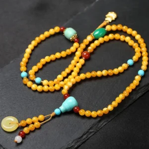 Flat lay of complete Tibetan prayer mala featuring gourd charm turquoise beads red agate and amber with gold pendant on dark background