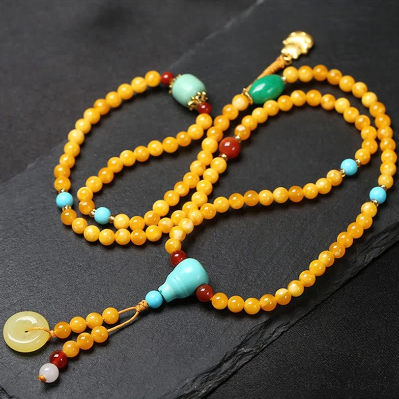 Flat lay of complete Tibetan prayer mala featuring gourd charm turquoise beads red agate and amber with gold pendant on dark background