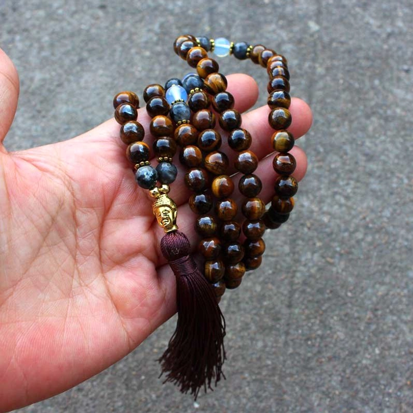 First-person view of tiger eye Buddha mala held in hand showing texture and gold charm detail