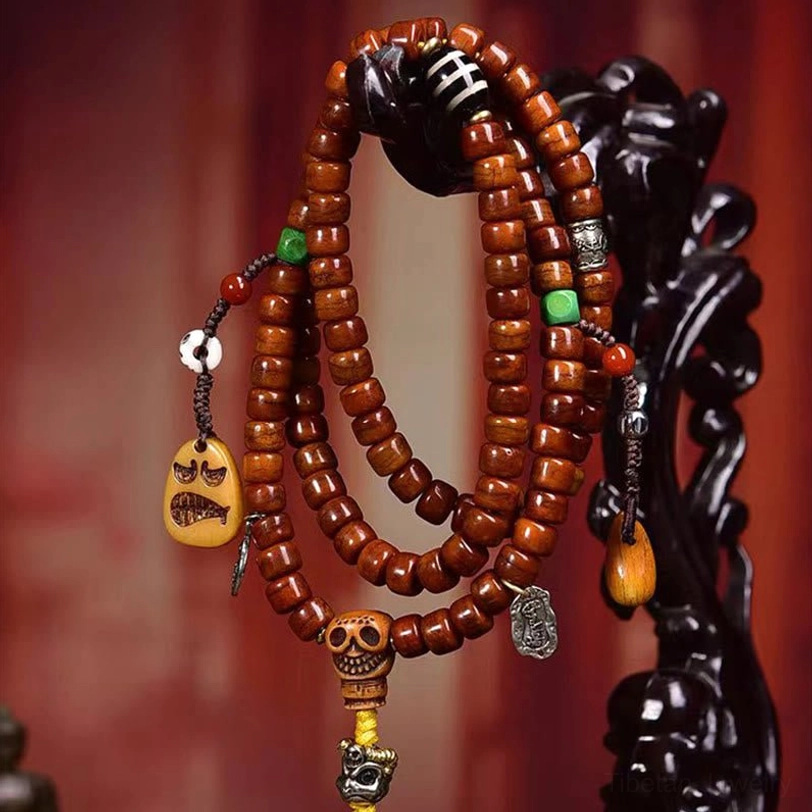 Tibetan bone bead prayer mala hanging on dark decorative stand showing reddish-brown beads with skull pendant and yellow tassel charm
