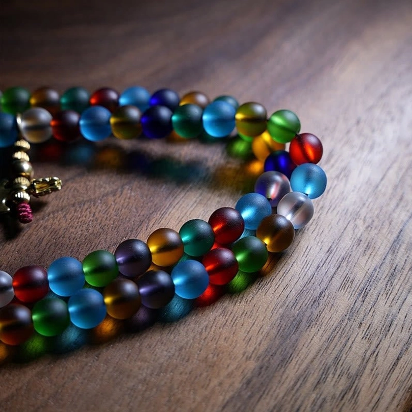 Looped Tibetan mala bead strand with vibrant rainbow colored glass beads and metal clasp pendant, side angle view