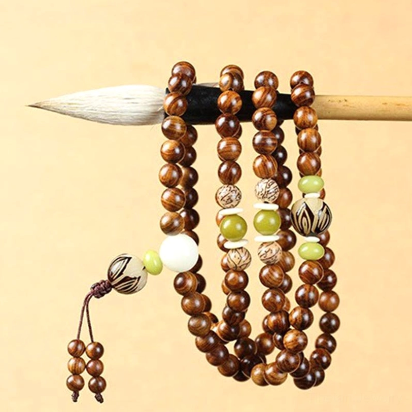 Long wooden prayer mala hung on traditional writing brush, showing complete strand with mixed accent beads and woven tassel against studio background