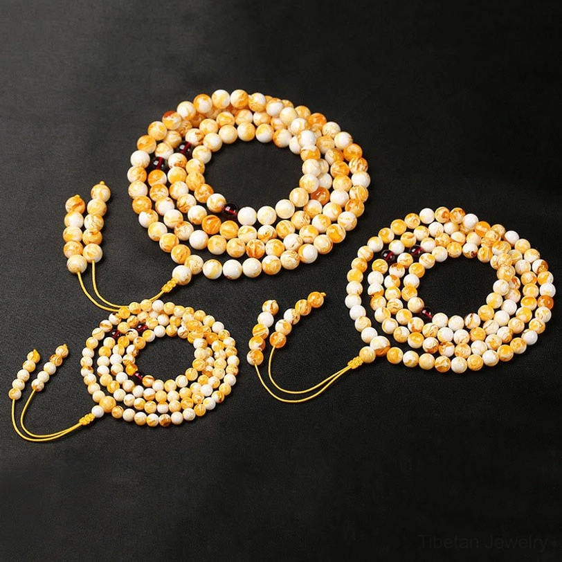 Four sets of Tibetan mala prayer bracelets with small round yellow beads and yellow tassel pendants on black fabric, flat lay view