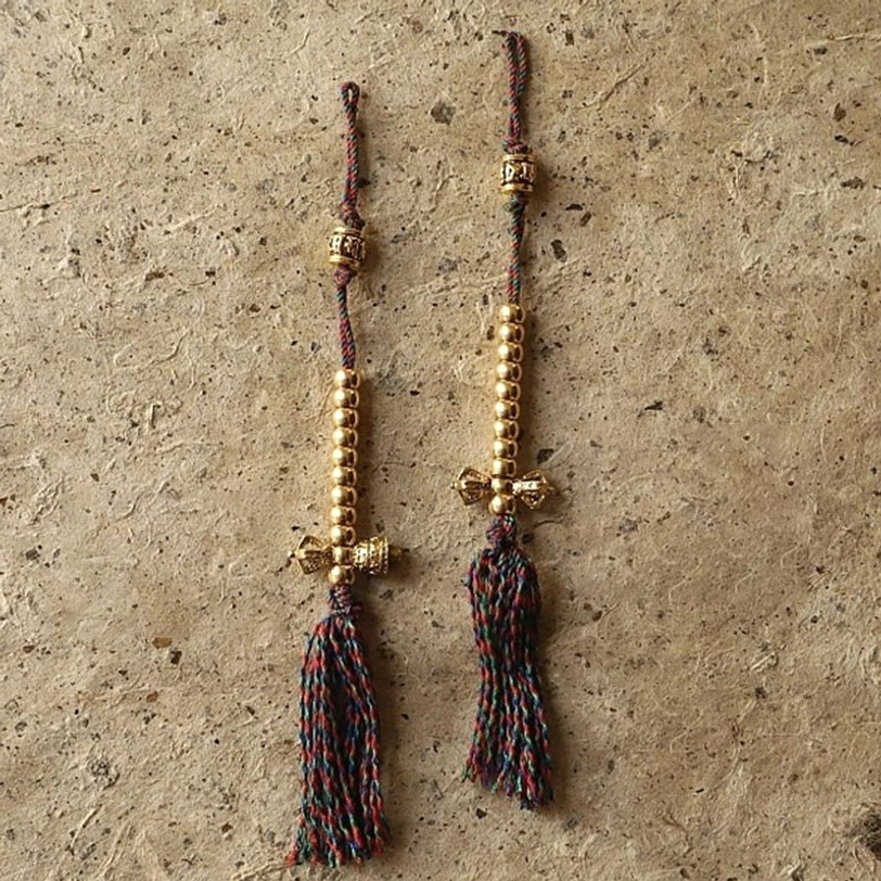 Tibetan Buddhist mala prayer counter beads with gold prayer wheel charms, mixed-color braided cords, and tassel pendants on concrete texture