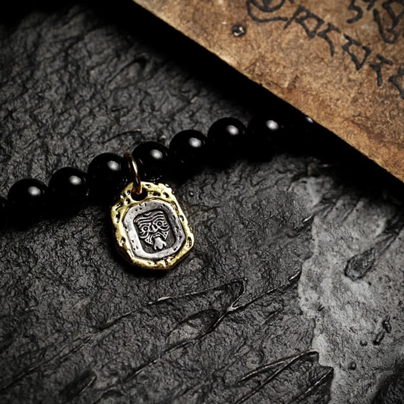 Tibetan mala protective pendant featuring embossed brass beast face amulet with black onyx and antique silver accent on dark stone with Tibetan script