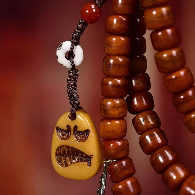 Side angle close-up of Tibetan dzi bead mala showing reddish-brown barrel beads with angry face pendant and white skull charm