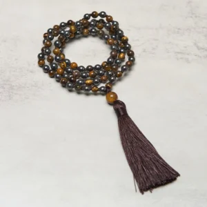 Tiger Eye and Hematite 108 bead mala necklace with brown tassel laid out on light gray background, showing mixed stone beads in warm brown and metallic tones
