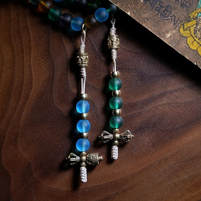 Mala bead decorative strand with silver metal ritual charms and gradient glass beads on Tibetan pattern decor board