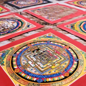 Multiple handcrafted Tibetan mandala thangkas with red borders displayed on workshop table - overhead view