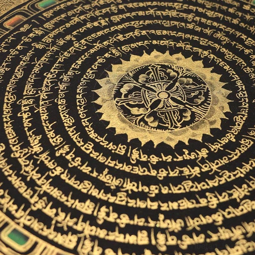 Extreme close-up of black and gold Tibetan mandala thangka showing hand-painted central sacred floral pattern surrounded by Tibetan scripture