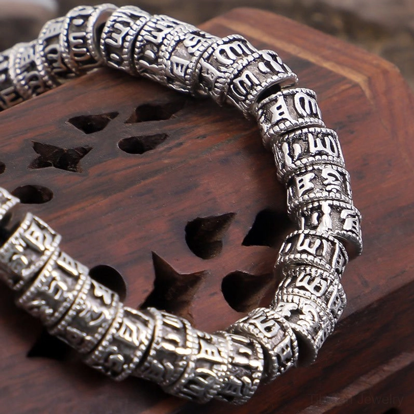 Close-up detailed view of Tibetan Om Mani Padme Hum mantra engravings on silver beads with rustic metal texture on wooden base