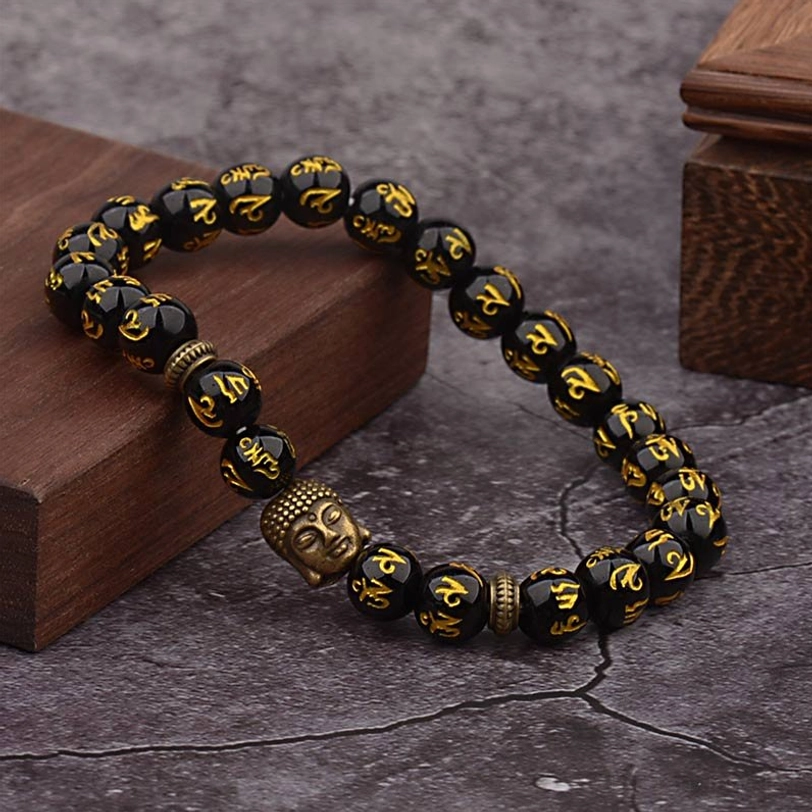 Tibetan mantra beaded bracelet with antique bronze Buddha charm, black beads, and gold-etched Sanskrit characters in natural setting