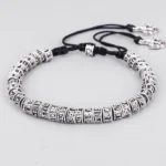 Handmade Tibetan Om Mani Padme Hum mantra bracelet with silver engraved beads and black adjustable cord, overhead flat lay on white background