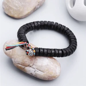 Handcrafted Tibetan mantra bracelet three-quarter side view with natural stone backdrop, black engraved coconut beads and silver decorative charm