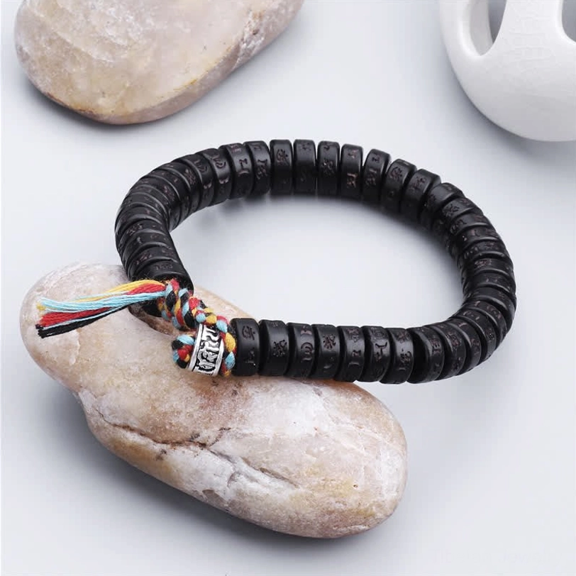 Handcrafted Tibetan mantra bracelet three-quarter side view with natural stone backdrop, black engraved coconut beads and silver decorative charm
