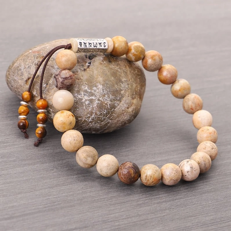 Natural stone Tibetan bracelet with beaded tassel on textured background, close-up of mantra charm and stone bead quality