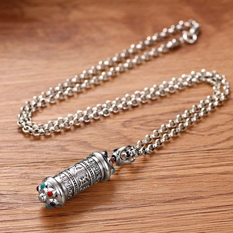 Tibetan mantra necklace full length layout showing silver curb chain and engraved pendant with colored gemstone details, flat lay top view