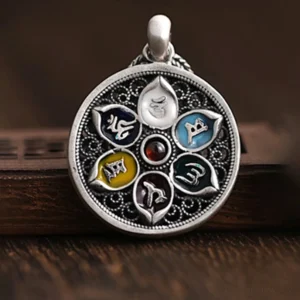 Tibetan round mantra pendant with antique silver finish, central red gem, and multicolored enamel inlays on wooden surface