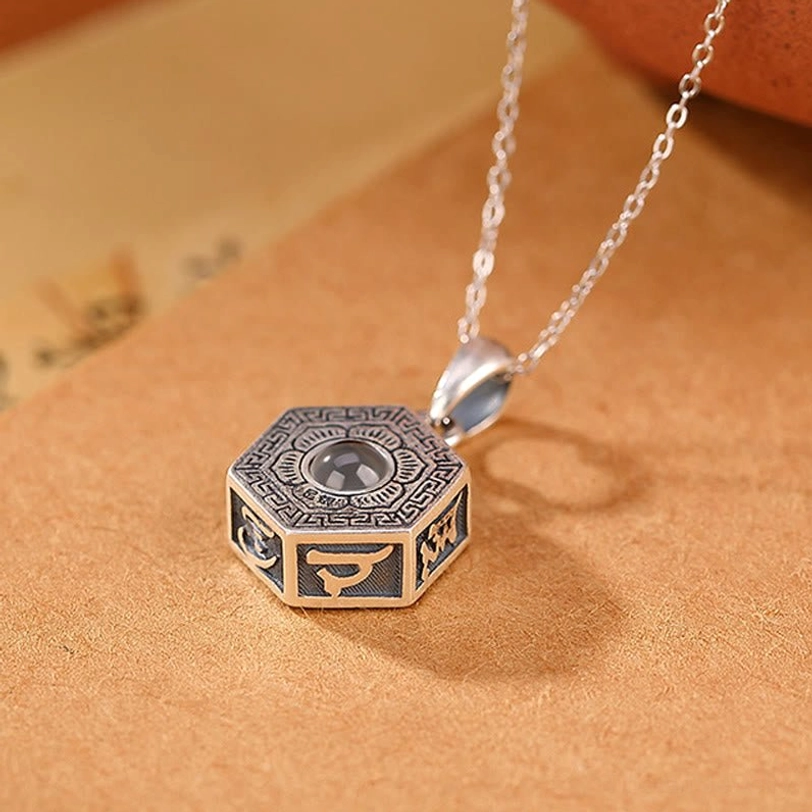 990 sterling silver Tibetan mantra pendant front low-angle view displaying engraved Sanskrit and Tibetan script on octagonal face with plain vintage paper background