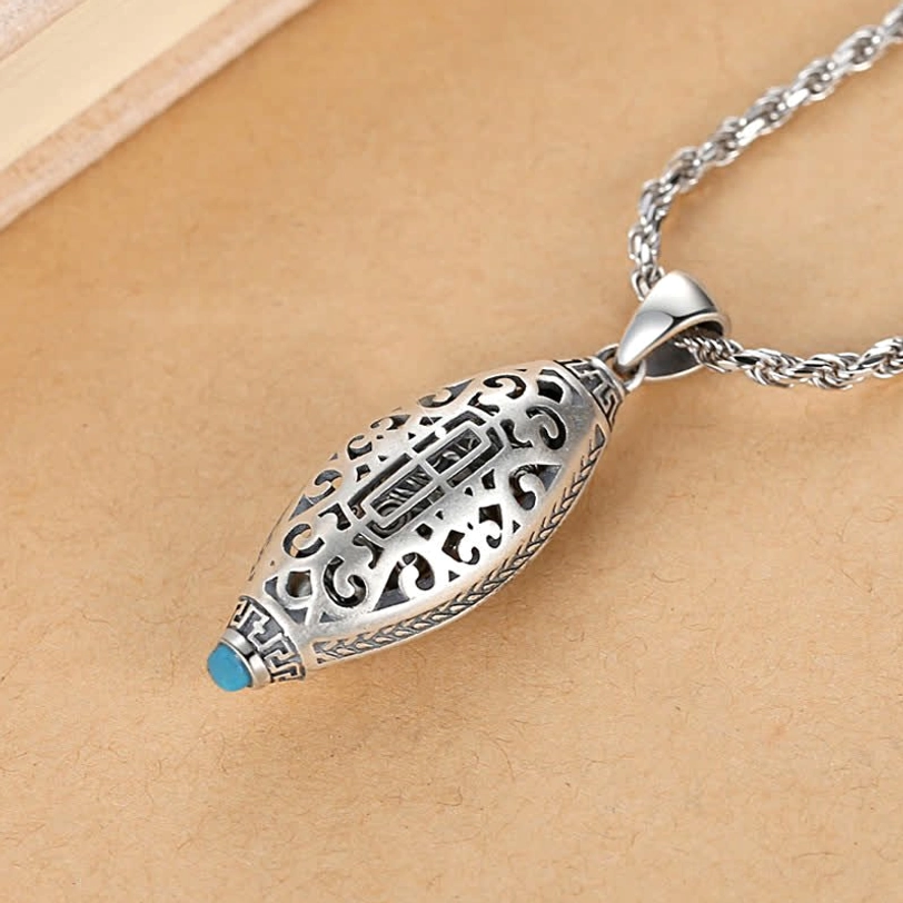 Openwork Tibetan Om Mani Padme Hum pendant necklace showing hollow carved patterns and blue bottom gem detail on light wood background