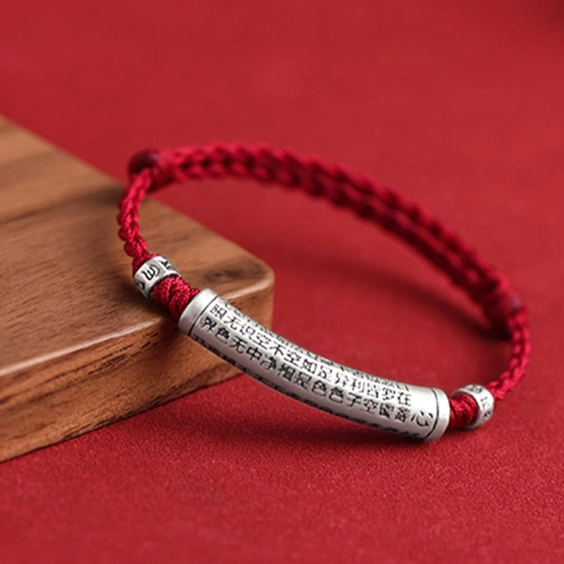 Tibetan Om Mani Padme Hum silver bracelet with engraved Buddhist scriptures displayed on red background with wooden prop