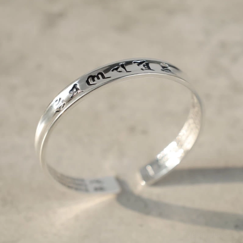 White copper Tibetan mantra bracelet oblique angle showing curved open cuff design with engraved Sanskrit mantras