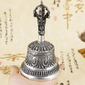 Single handcrafted Tibetan meditation bell held in hand showing vajra finial top and elaborate relief engravings on calligraphy desktop background