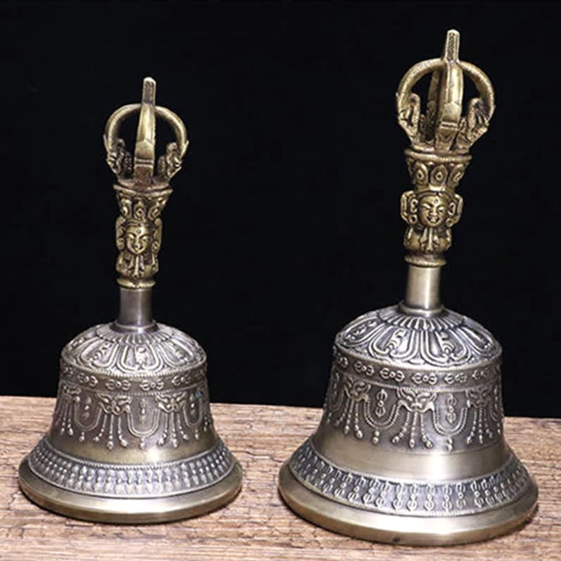 Two matching Tibetan meditation bells with embossed decorative patterns, aged bronze and silver-grey finish on wooden table