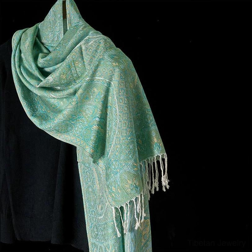 Mint green Tibetan jacquard tassel shawl with floral geometric woven pattern and white fringe trim, displayed in three-quarter draped view