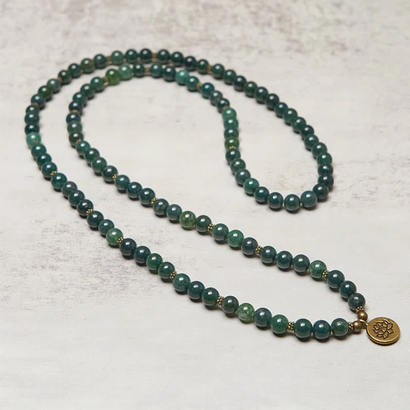 Full-length moss agate 108-bead mala with lotus charm, strung meditation necklace lay flat on light background