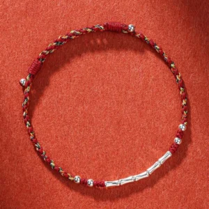 Handmade Tibetan multicolor braided protection bracelet with red and yellow threads and silver copper bead, overhead view on terracotta background