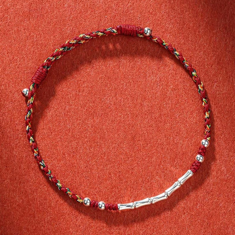 Handmade Tibetan multicolor braided protection bracelet with red and yellow threads and silver copper bead, overhead view on terracotta background