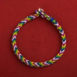Five-color braided Tibetan protection bracelet with alloy clasp, flat lay top-down view on red background
