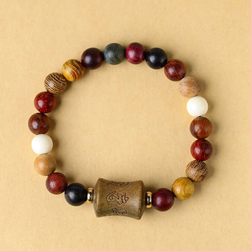 Tibetan style multicolored sandalwood beaded bracelet overhead view on wooden table showing engraved central barrel bead and natural wood assortment
