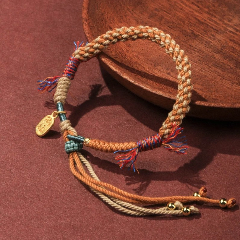 Hand-woven Tibetan luck bracelet flat lay showing frayed colorful tassels and adjustable rope ends with Fu charm