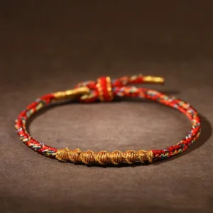 Handmade red and gold twisted Tibetan zodiac natal buddha braided string bracelet with adjustable knot closure on dark background