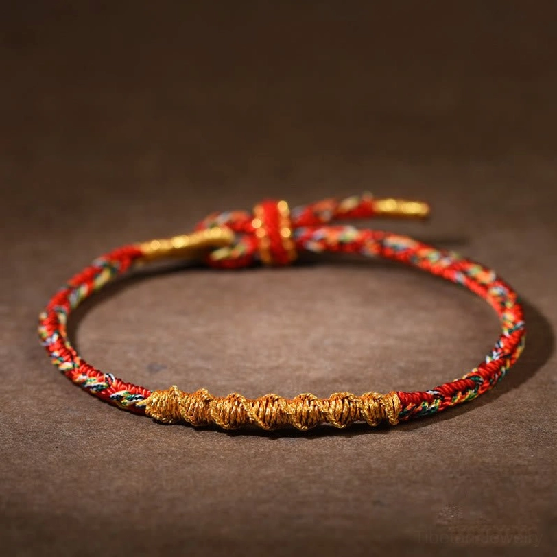 Handmade red and gold twisted Tibetan zodiac natal buddha braided string bracelet with adjustable knot closure on dark background