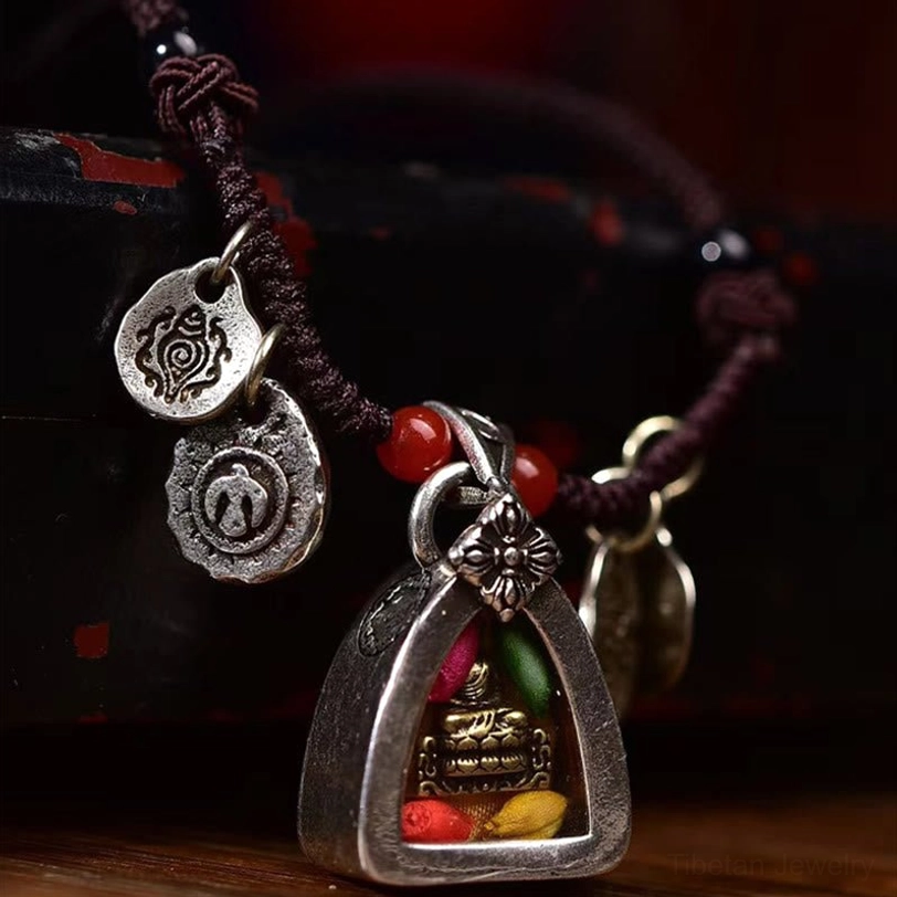 Side view of braided Tibetan buddha necklace featuring engraved silver pendants, red accent beads, and natural brown cord against wooden background