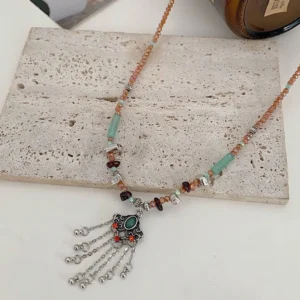 Flat lay top-down view of Tibetan tassel necklace with brown beaded chain, green jade beads, and enamel decorated copper pendant on stone background
