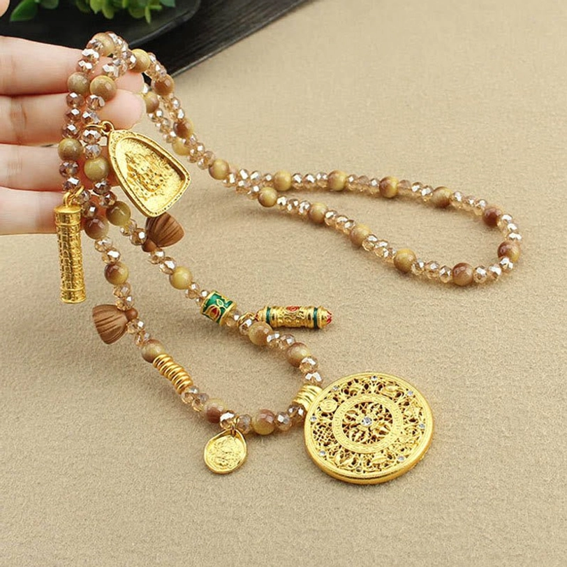 Close-up detail of Tibetan lotus necklace held in hand showing tiger eye beads and gold charms