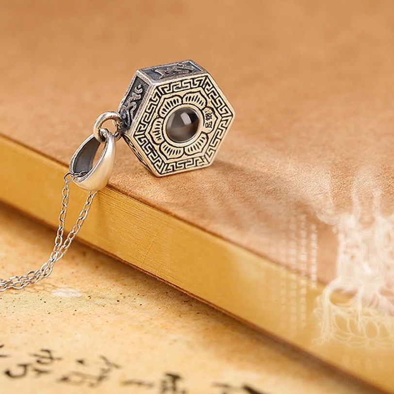 Tibetan silver necklace side view displaying Tibetan script engravings on pendant sides with attached chain on vintage stationery background