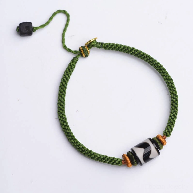 Tibetan dzi bead nine-eye protection bracelet with green braided cord and adjustable closure, lifestyle flat lay