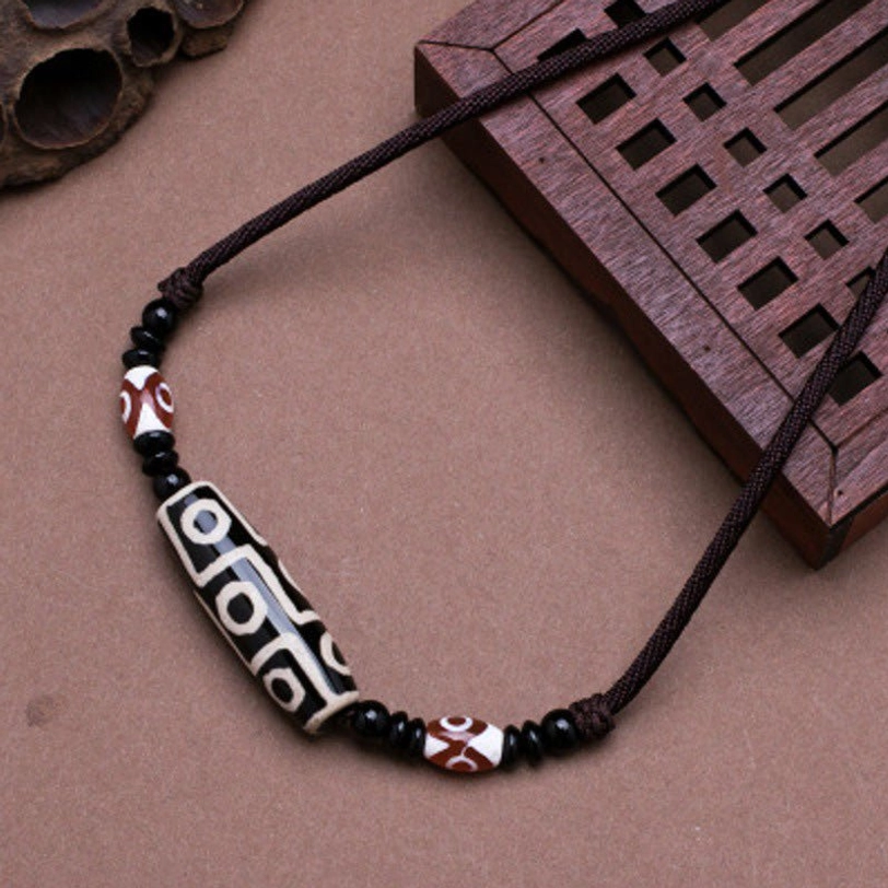 Black Tibetan nine-eye dzi bead necklace with black wax cord on carved wooden board - close-up view of protective amulet pendant