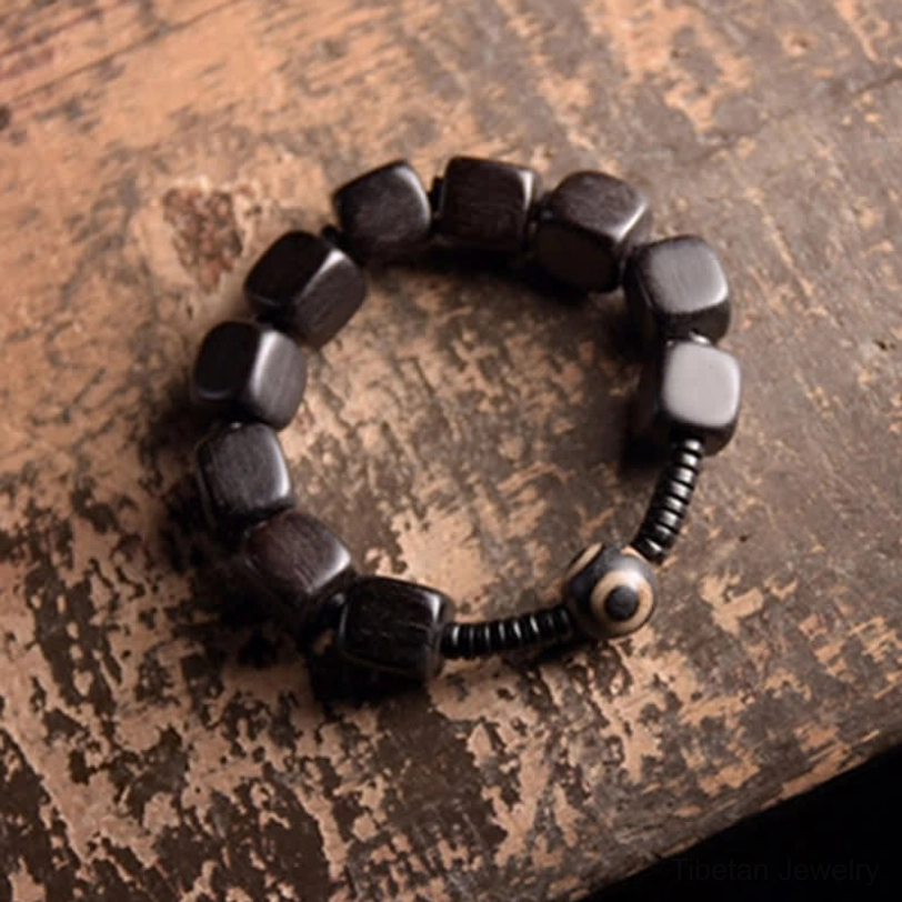 Tibetan protective dzi bead bracelet handmade with cuboid ebony wood beads and traditional nine-eye dzi accent bead on weathered wood