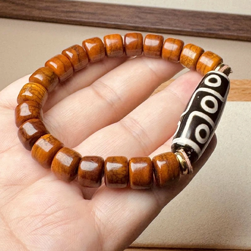 Tibetan nine-eye Dzi bone bracelet with metal clasp worn on hand against wooden background
