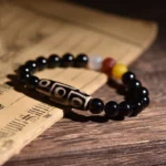 Tibetan nine-eye dzi bead bracelet shown from overhead on antique scroll, featuring black agate beads with classic nine-eye etched pattern and colorful spacer beads