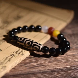 Tibetan nine-eye dzi bead bracelet shown from overhead on antique scroll, featuring black agate beads with classic nine-eye etched pattern and colorful spacer beads