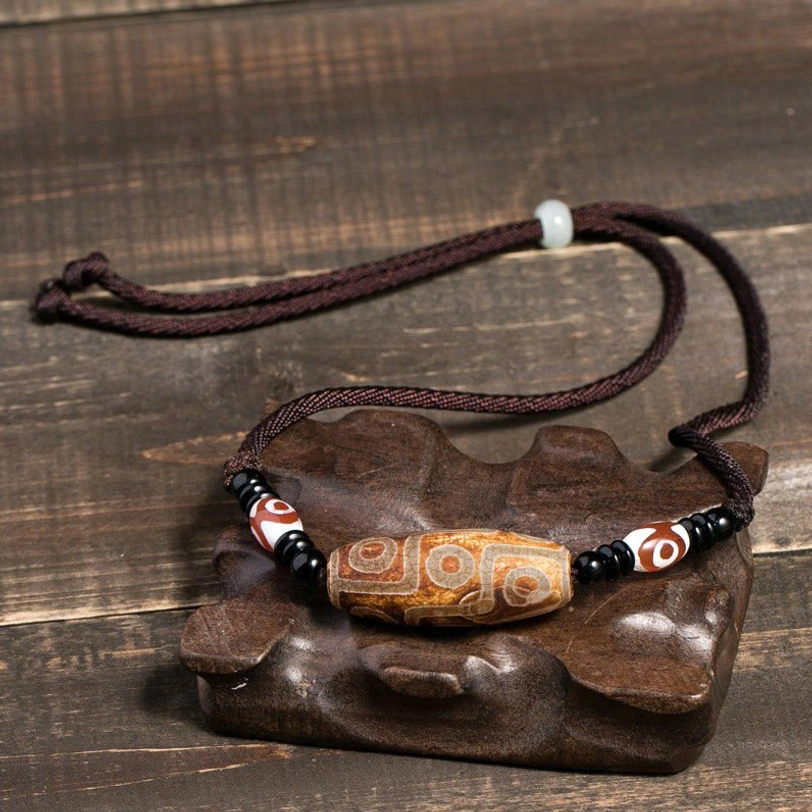 Brown Tibetan nine-eye dzi bead necklace on wooden display stand with adjustable cord - wealth and prosperity protection pendant